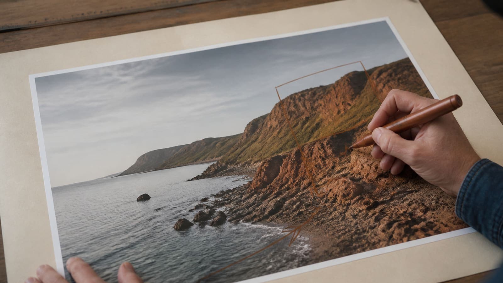 Hands cropping a large original print file on a cream desk with a copper focal marker