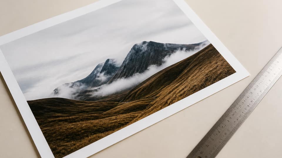A JPEG print file proof beside a paper print on a cream desk, metal ruler, no readable filenames